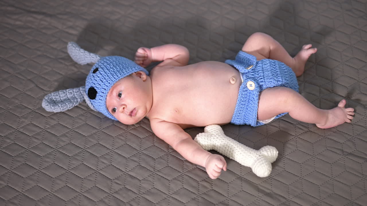 Sweet baby lying on the big bed in a costume of a puppy. Naked baby in the diaper and cap on the bed. View from above.