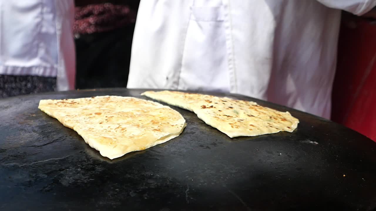 Person preparing flatbread on a large griddle