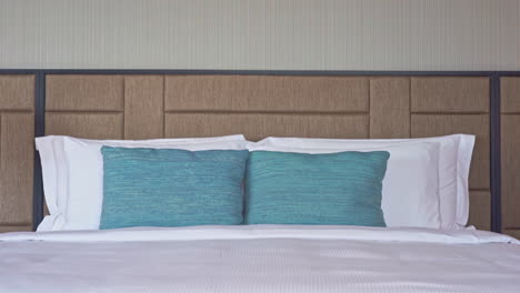 tiro inclinado hacia abajo que revela una cama tamaño king en una habitación de hotel, con sábanas y almohadas blancas y dos cojines verde esmeralda