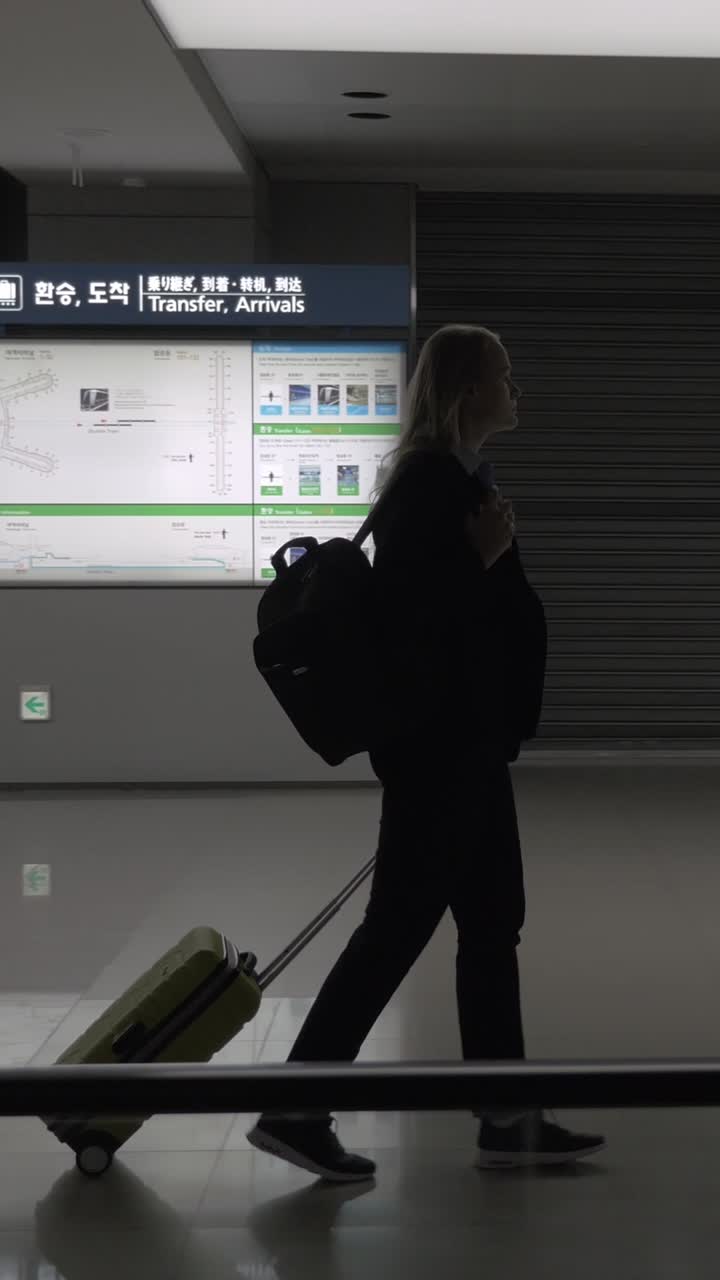Silueta de una mujer caminando con equipaje en una concurrida terminal de aeropuerto