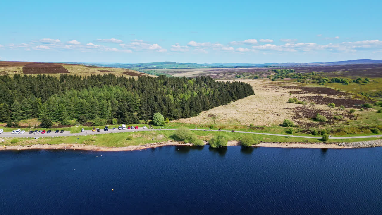 The picturesque Winscar Reservoir in Yorkshire sets the stage for a dazzling boat race, as small one-man boats with white sails compete in the serene blue lake, basking in the radiant midday sunlight