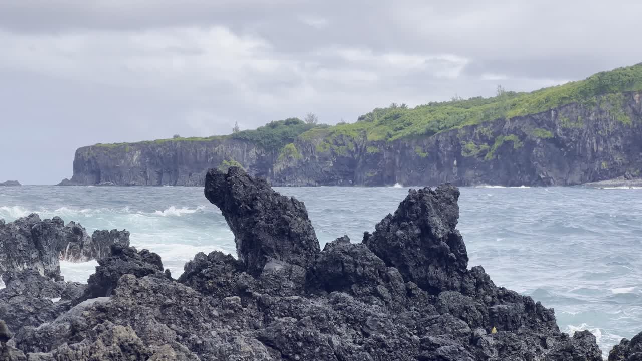 Cinematic booming up shot of rough waves crashing into lava rock along the Road to Hana in Maui, Hawai'i