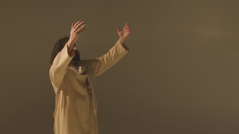 three quarter length studio portrait of man wearing robes and sandals with long hair and beard representing figure of jesus christ praying