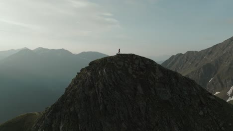 aerial drone shot pulling back on a man hiking over a scenic mountain hill in the alps