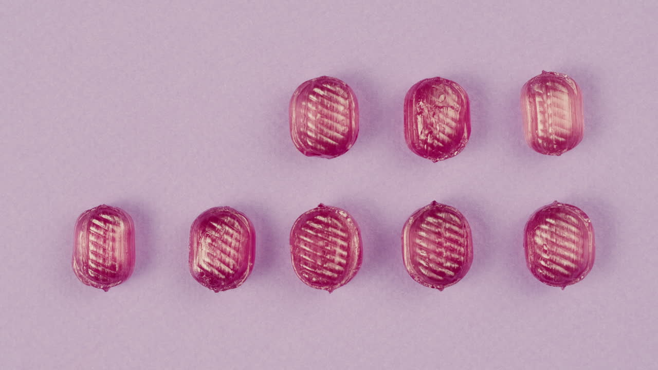 Pink lollipops, candies, bonbons appear on purple background. Summer bright texture studio shot for store, supermarket, close up top view. Children's favorite sweets made of sugar.