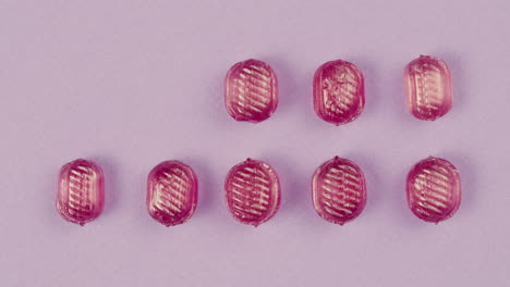pink lollipops, candies, bonbons appear on purple background. summer bright texture studio shot for store, supermarket, close up top view. children's favorite sweets made of sugar.