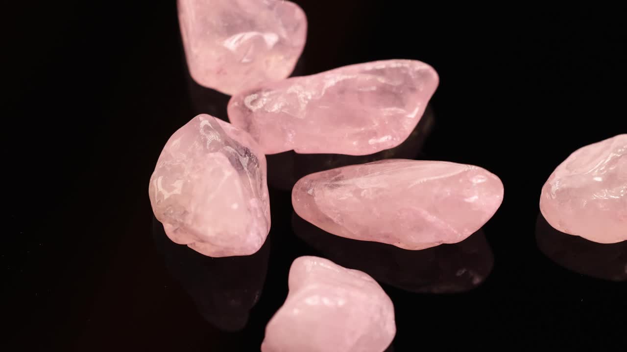 Rose quartz stones spin on a glossy black surface, creating a mesmerizing visual effect with soft lighting and gentle reflections