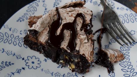 baked-brownie-dessert-slice-topped-with-meringue-with-chocolate-syrup-being-drizzled-on-top