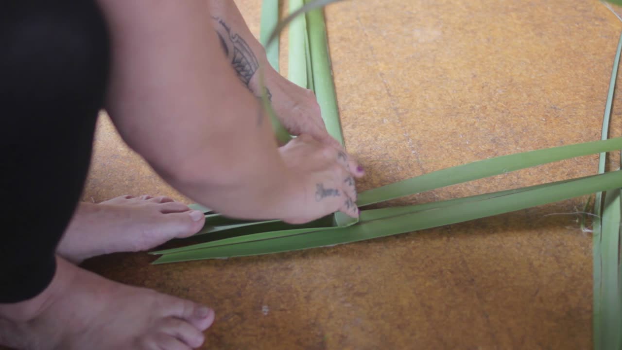 여성의 발과 식물 잎을 사용하여 마오리 전통 방식으로 바구니를 만들고 있는 모습