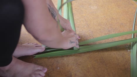 primer plano de una canasta hecha de manera tradicional maorí usando los pies de una mujer y hojas de plantas.