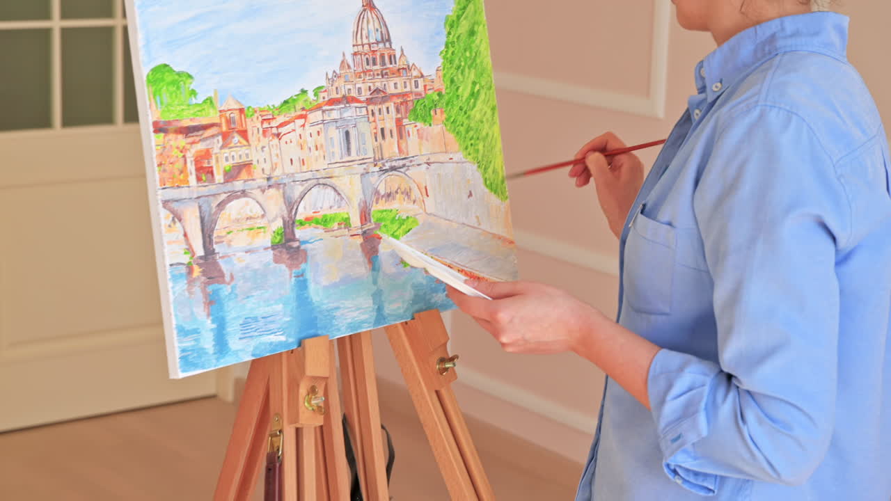 Woman painting picture on the easel holding a palette at home