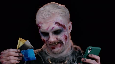 sinister man halloween zombie using credit bank cards and smartphone while purchases online shopping