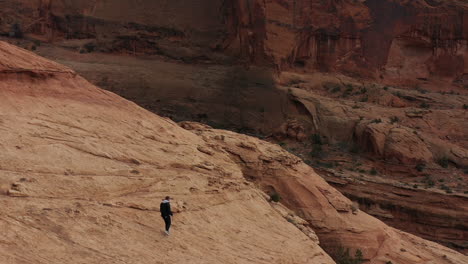 aerial view of male running on hillside of sandstone hills in utah desert, tracking drone shot