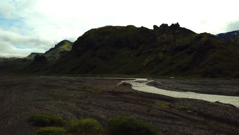 Aerial-landscape-view-of-people-hiking-towards-a-bridge,-crossing-a-river-flowing-in-the-FimmvÃ¶rÃ°uhÃ¡ls-area,-Iceland