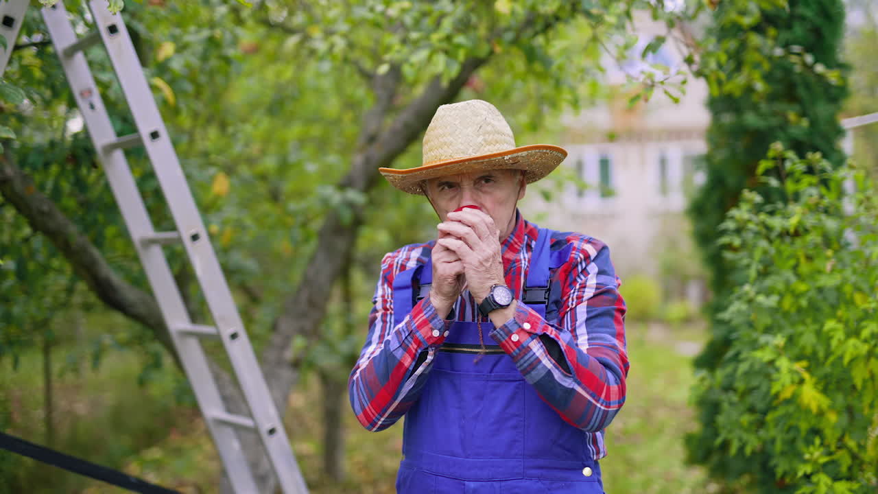 Male gardener in hat holding a fresh ripe apple outdoors. Farmer sniffs aromatic apple in the garden in autumn. Organic food.