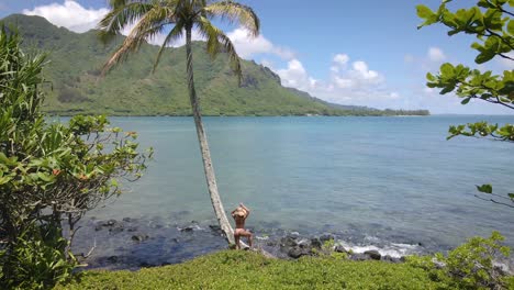 Beneath-the-shade-of-a-palm-tree,-a-woman-in-a-pink-bikini-and-straw-hat-graces-a-Hawaiian-beach