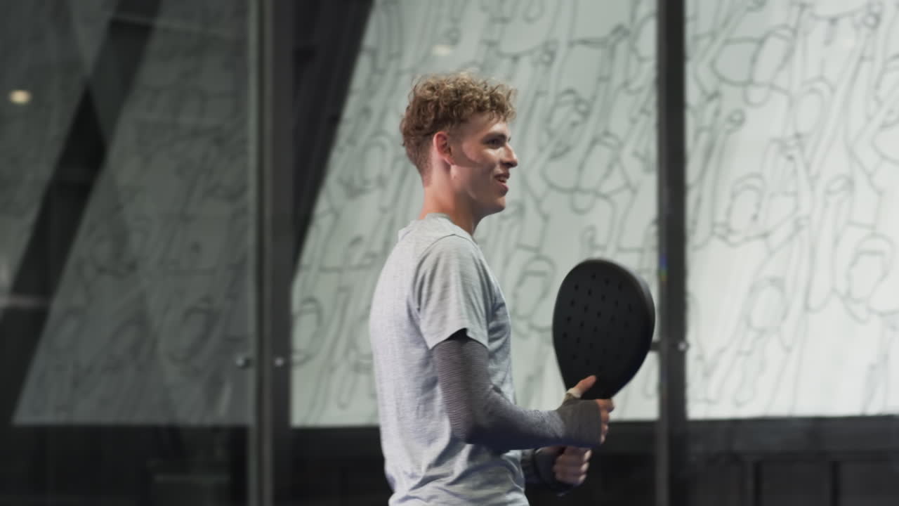 Young man playing padel tennis on indoor court, holding racket and looking focused