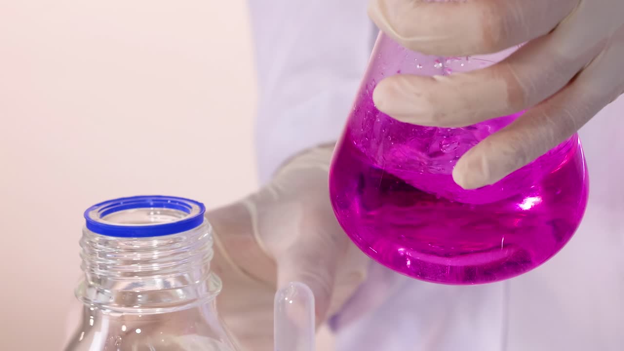 A gloved hand mixes a vibrant pink solution in a laboratory flask.
