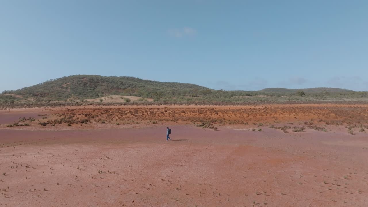 Uzak Avustralya taşra bölgesinde yürüyen bir adamı gösteren geniş açılı kaydırmalı drone çekimi.