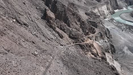 aerial remote surveillance view of winding old silk road through rugged arid mountains beside river