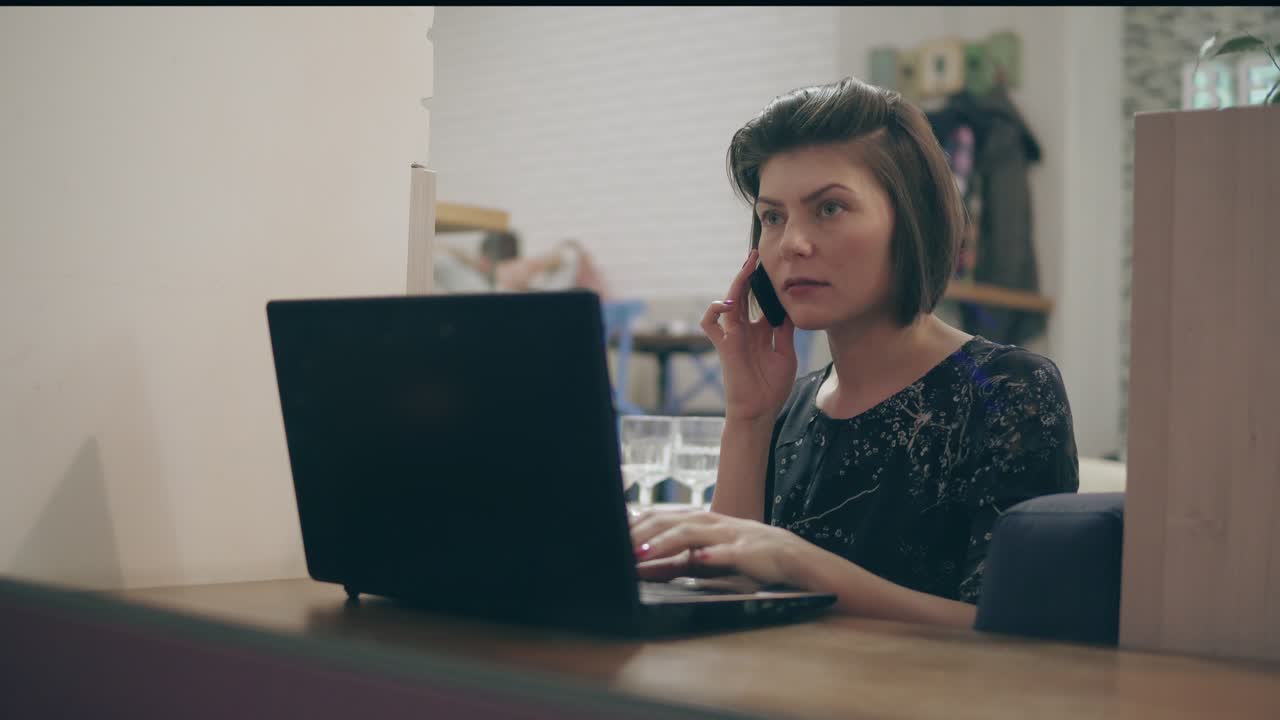 Young business woman sitting by the window with a laptop and talking on the phone