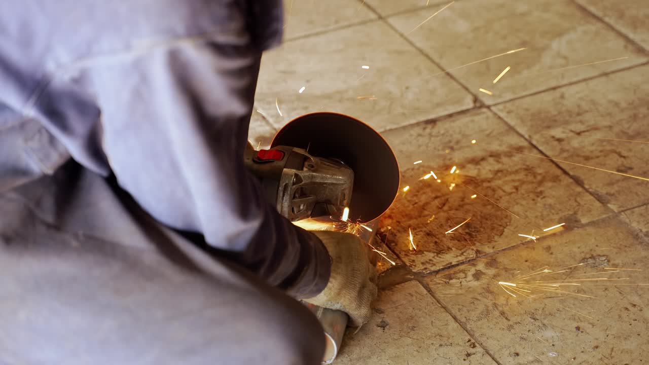 un trabajador corta un tubo en el suelo con una molienda angular. las chispas naranjas vuelan en diferentes direcciones
