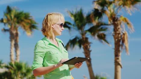 una mujer con una camisa verde claro que usa una tableta contra el cielo y las palmeras