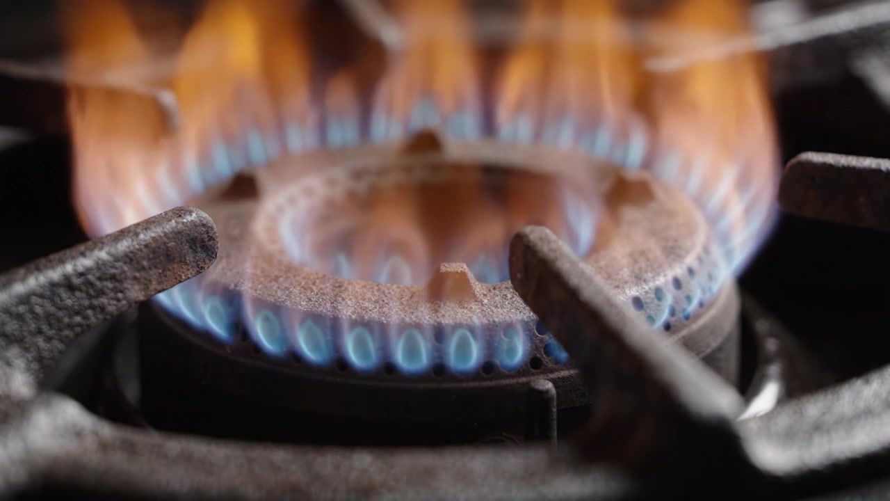 A Close-Up View of a Gas Burner Igniting with a Vivid Blue Flame as a Cooking Pot Sits Above, Showcasing the Intensity and Precision of Home Cooking.