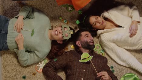 looking down on group of friends lying on floor dressing up with irish novelties and props at home for st patrick's day party 1