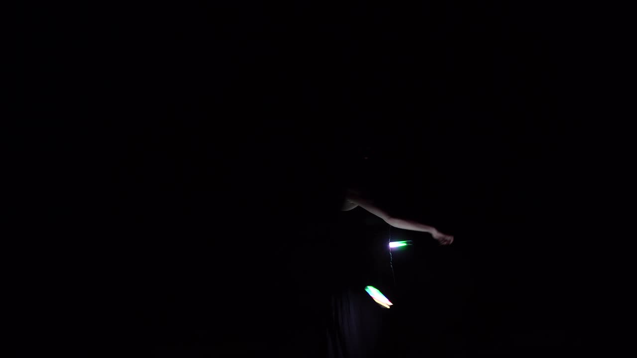 una chica morena en la oscuridad muestra un espectáculo de fuego.