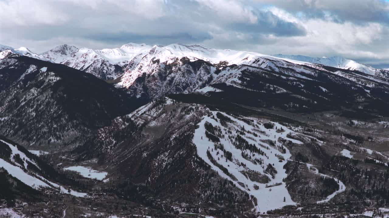 Panorama invernale e primaverile del comprensorio sciistico Buttermilk e della Maroon Bells Wilderness, con veduta aerea da drone della località sciistica di Aspen Snowmass in una mattinata invernale soleggiata e nuvolosa. Riprese delle piste da sci del Colorado con movimento circolare a destra verso Pyramid Peak.