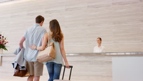 Attractive-happy-couple-arriving-at-hotel-reception-travelling-on-vacation