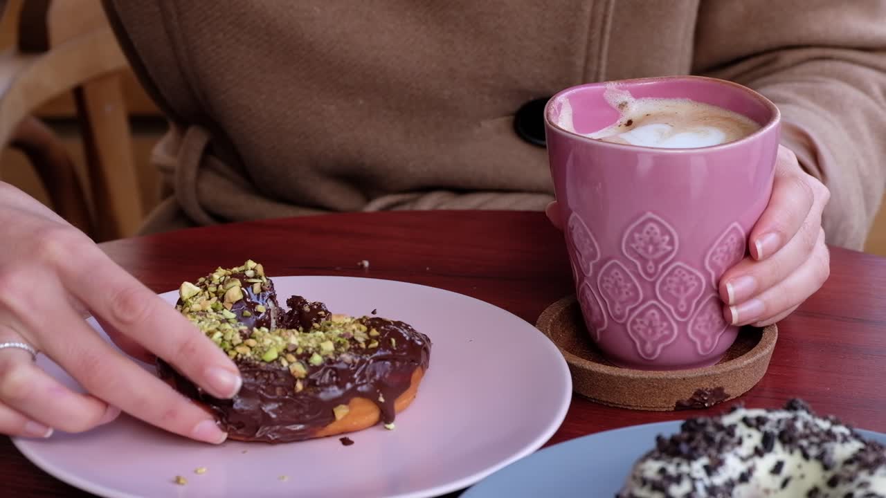 Close up of a woman in a brown coat eating donuts and drinking coffee at a cafe