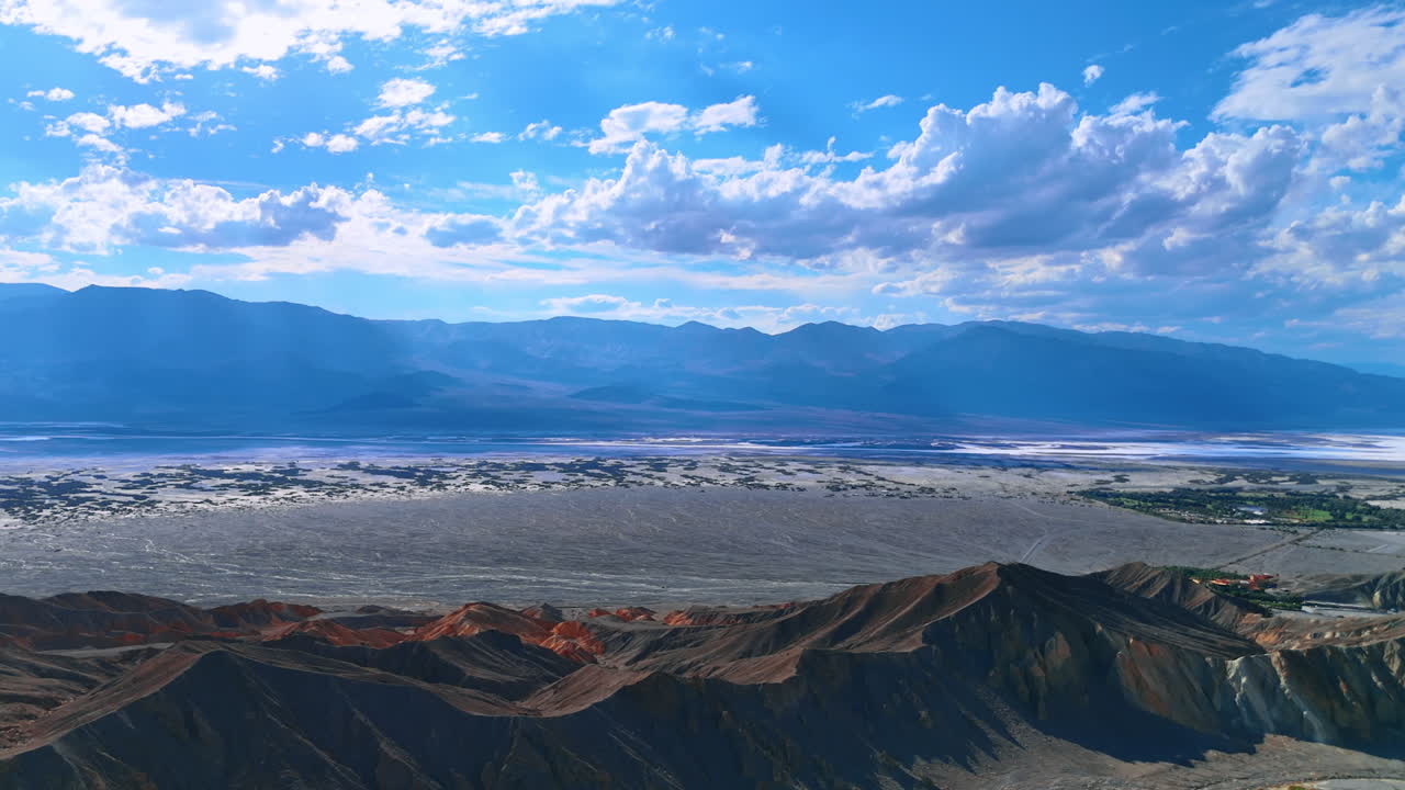 Flight over the ridged bare rocks in the Death Valley National Park, California, USA. Beautiful clouds gathered in the blue sky above