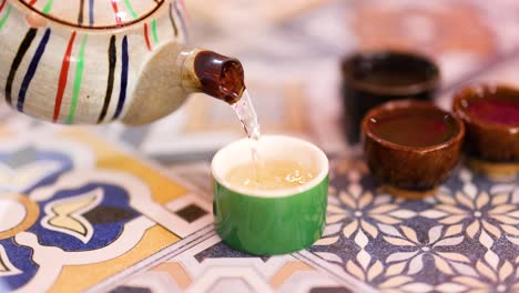 A teapot pours steaming tea into a cup on a vibrant, patterned tablecloth, creating a warm, inviting atmosphere