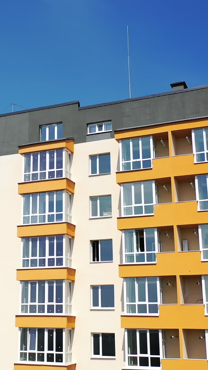New multi-storey building in the city. Contemporary apartment building with large windows and colorful walls of the facade of a new house for city residents on sky background. Vertical video