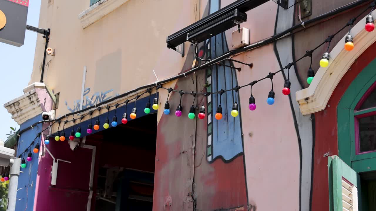 Camera pans over vibrant urban mural and string lights on colorful building facade in daylight