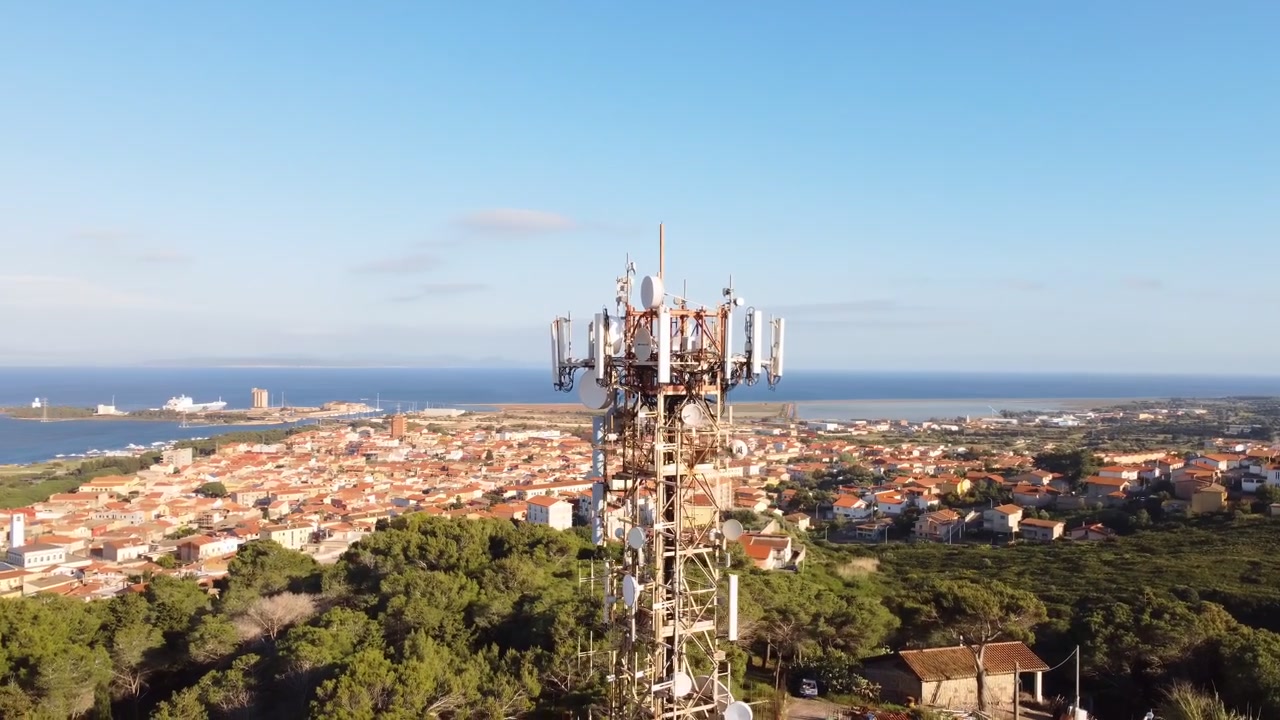 Drone aéreo circulando uma torre 5G no topo de uma colina em uma cidade litorânea, Sardenha