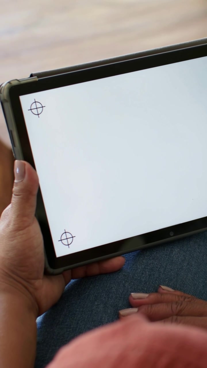 Vertical video: Tilt causing woman in coral top and jeans moving tablet for test, showing crosshair