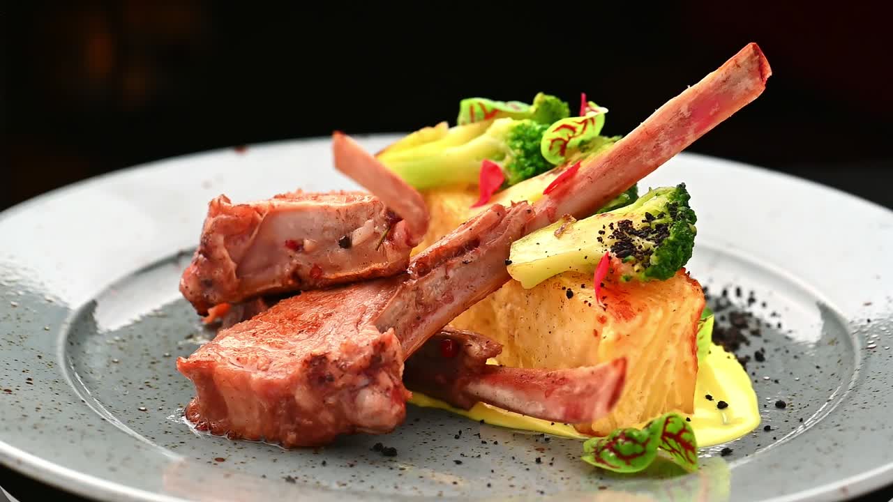 Restaurant serves grilled lamb chops with vegetables on a plate. Grilled lamb chops sit on a plate next to vegetables and garnishes in a restaurant setting