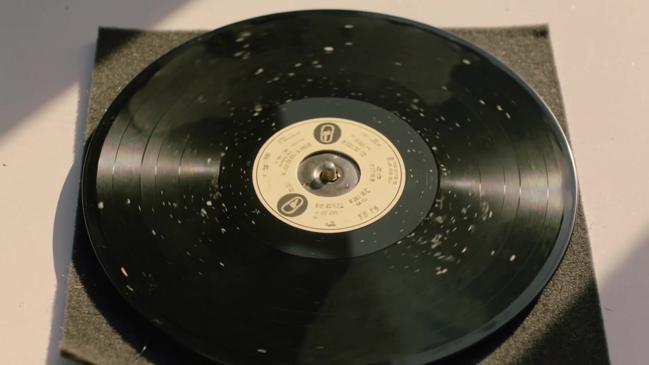 Un disco in vinile nero che gira su un tappetino di schiuma, con il perno che crea riflessi e scintille illuminate dal sole.