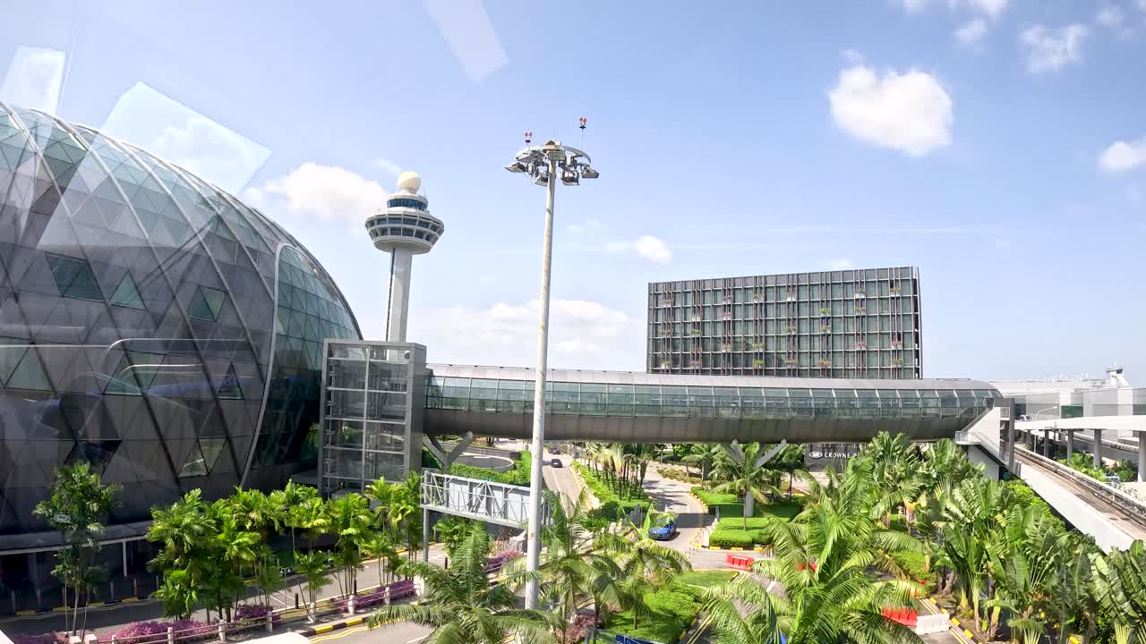 Wide daytime pan reveals modern glass dome, control tower, skybridge, lush greenery, and blue sky