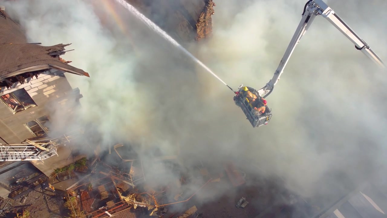 Vista dall'alto di un edificio in fiamme e fumante, con i vigili del fuoco che estinguono l'incendio con l'acqua e uomini coraggiosi sulla sommità dell'edificio