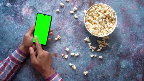 persona viendo una película en un teléfono inteligente con palomitas de maíz