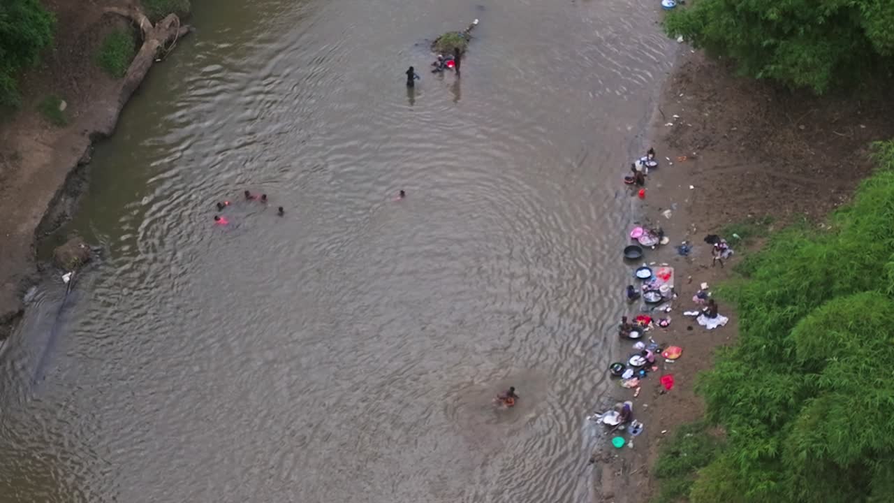 Authentiek tafereel uit het echte leven van kinderen die spelen in de wateren van de Massacre Rivier terwijl vrouwen kleding wassen