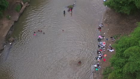 Authentische-Reale-Szene-Von-Kindern,-Die-Auf-Dem-Wasser-Eines-Massakerflusses-Spielen,-Während-Frauen-Kleidung-Waschen