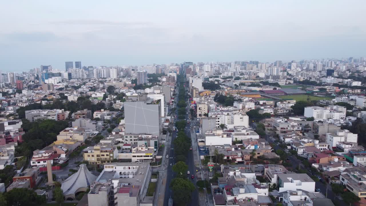 drone volando hacia adelante sobre una calle llamada "avenida benavides" con muchos árboles en medio de los 2 carriles, adentrándose en el horizonte lejano de la ciudad