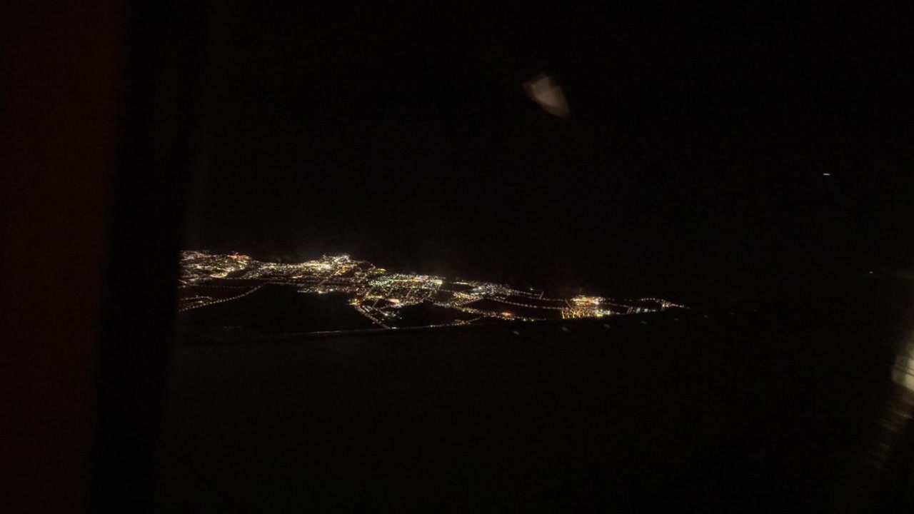 Vista dal finestrino dell'aereo delle luci urbane scintillanti di Lanzarote lungo la costa scura durante un volo notturno. Spazio per il testo.