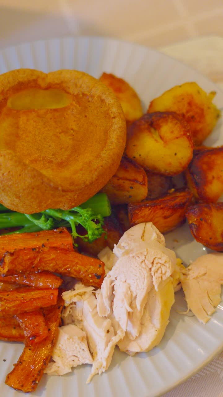 Video verticale: Cena arrosto britannica impiattata con pollo arrosto e verdure tra cui carote, broccoli, patate e guarnita con Yorkshire Pudding. Fotografia culinaria di cucina inglese