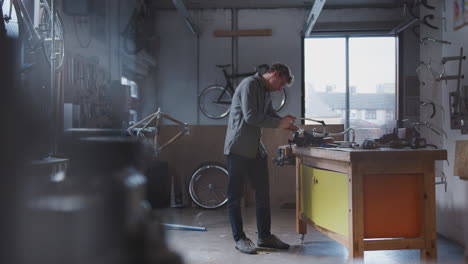 male business owner in workshop for building bicycles  sawing component in vice